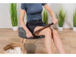 Ansicht auf eine Frau in Sportklamotten, die auf einem Sessel sitzend mit dem Styleholz Woodstick FLEX ihren rechten Oberschenkel behandelt