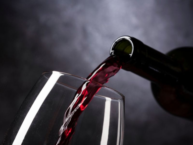 Rotwein, der aus einer Flasche in ein Glas eingeschenkt wird vor dunklem Hintergrund